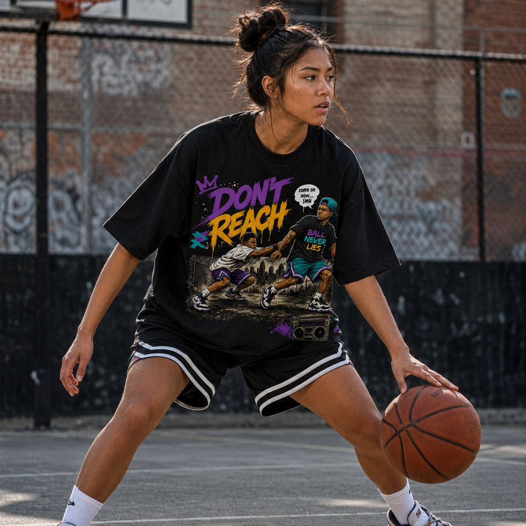Person playing basketball on an outdoor court wearing a black t-shirt with colorful graphics and text.