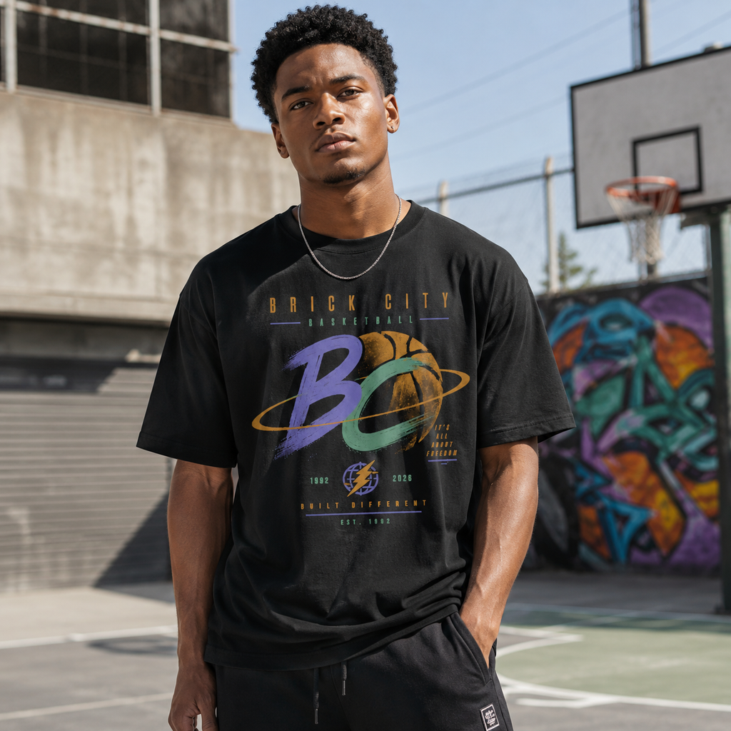 Man wearing a black t-shirt with 'Brick City Basketball' design on an outdoor basketball court.