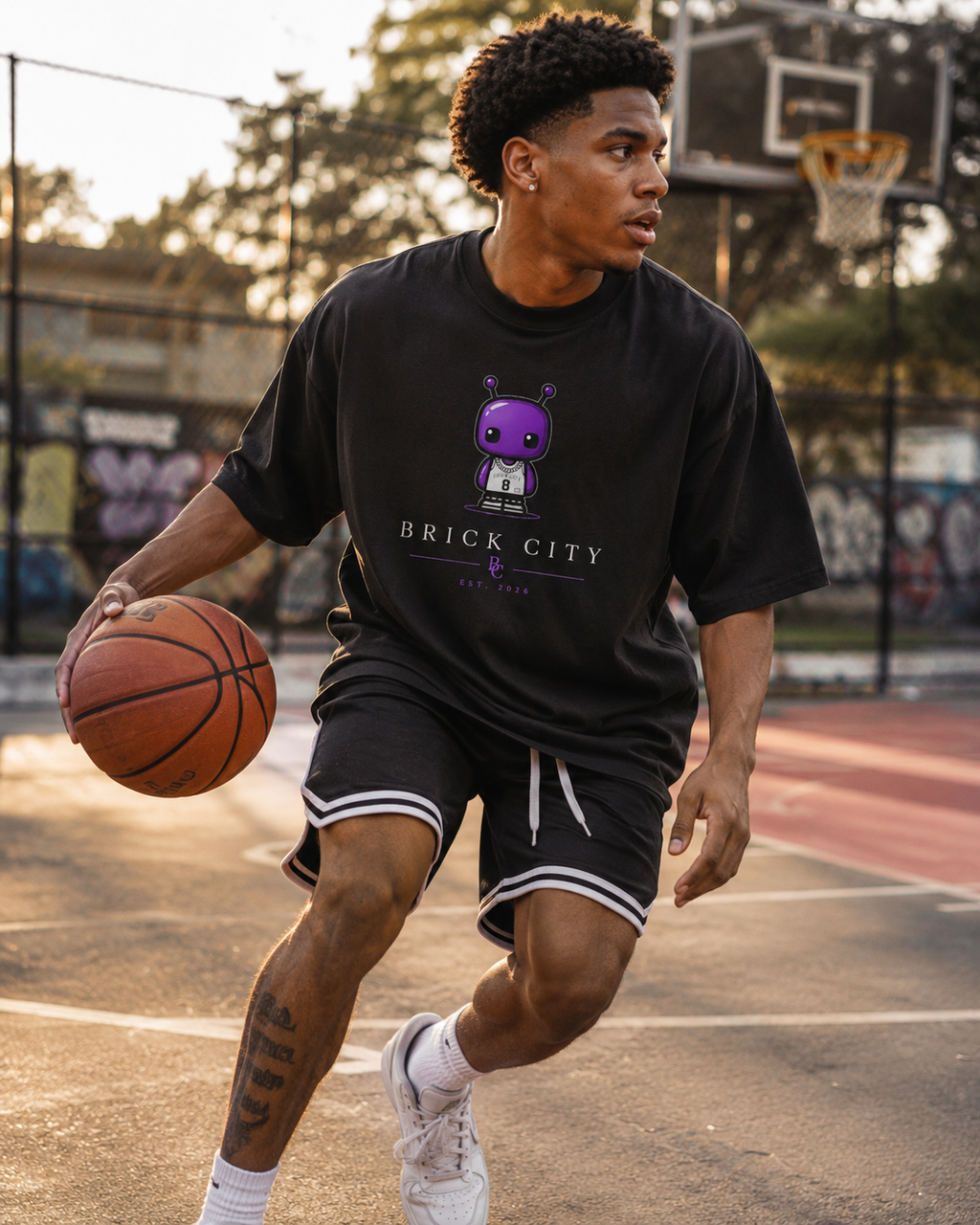 Person holding a basketball on a court wearing a black 'Brick City' t-shirt.