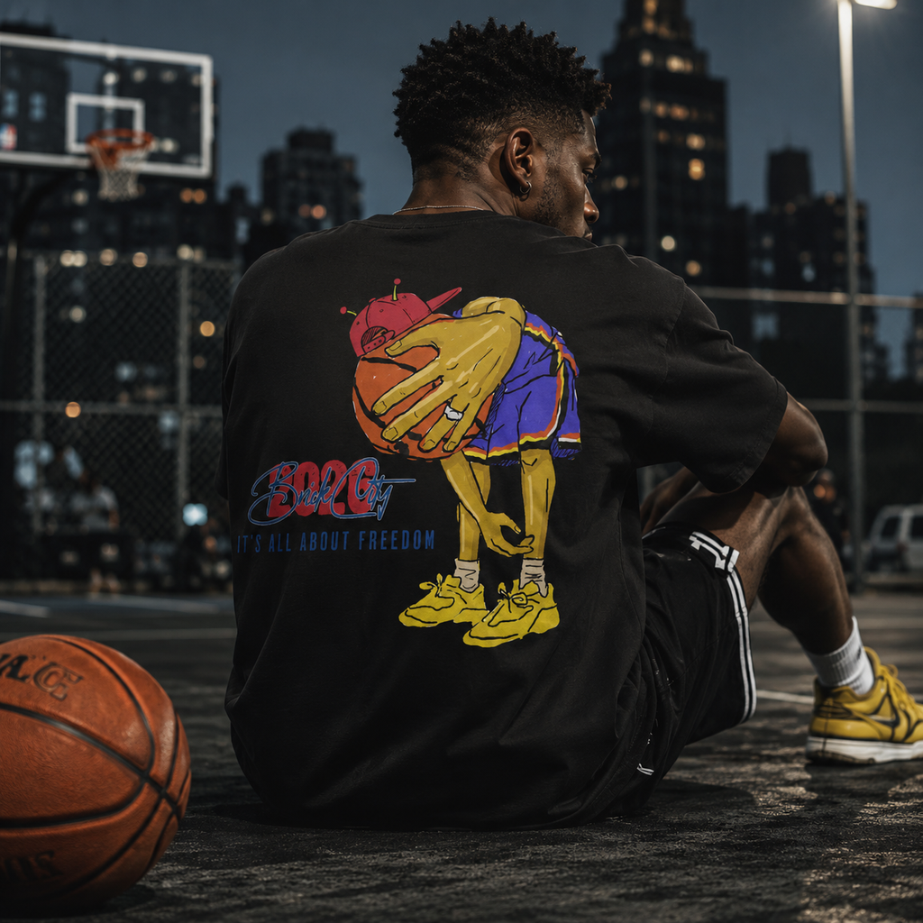Person sitting on a basketball court wearing a black sweatshirt with a colorful graphic, with a basketball next to them and cityscape in the background.