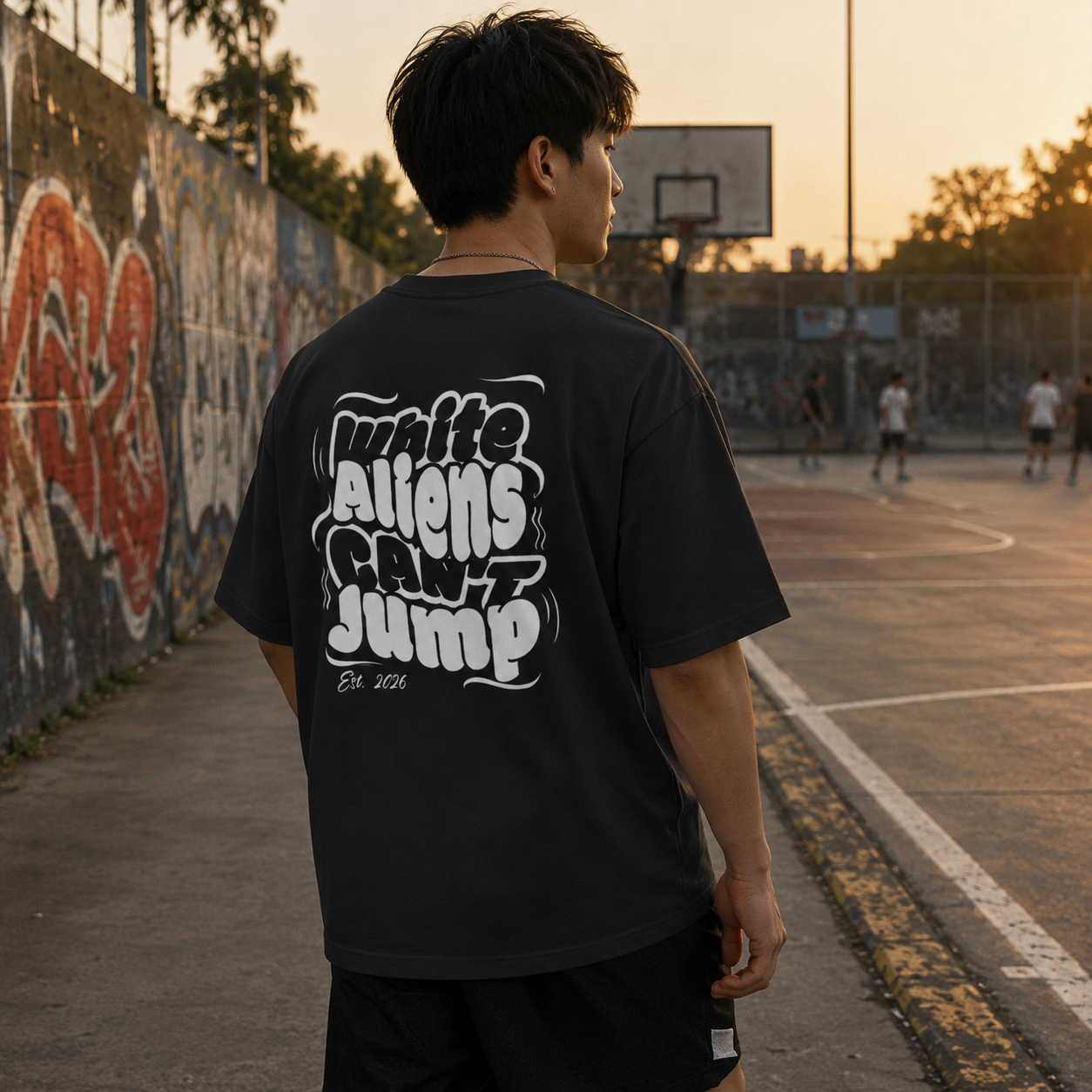 Person wearing a black t-shirt with white text on a basketball court at sunset.