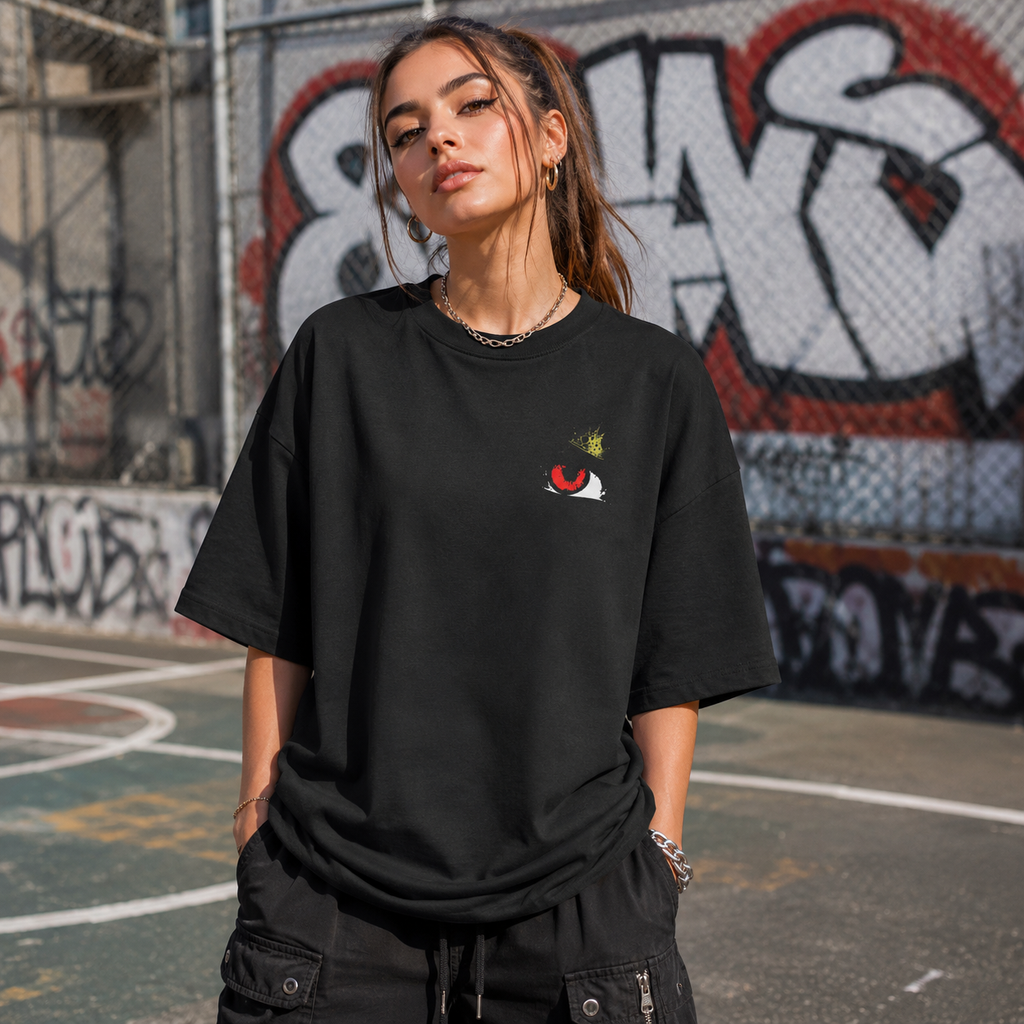 Person wearing a black oversized t-shirt with a small logo on a graffiti-covered wall background