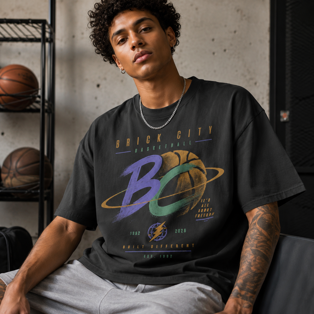 Person wearing a black t-shirt with 'Brick City Basketball' design, sitting in a room with basketballs on shelves