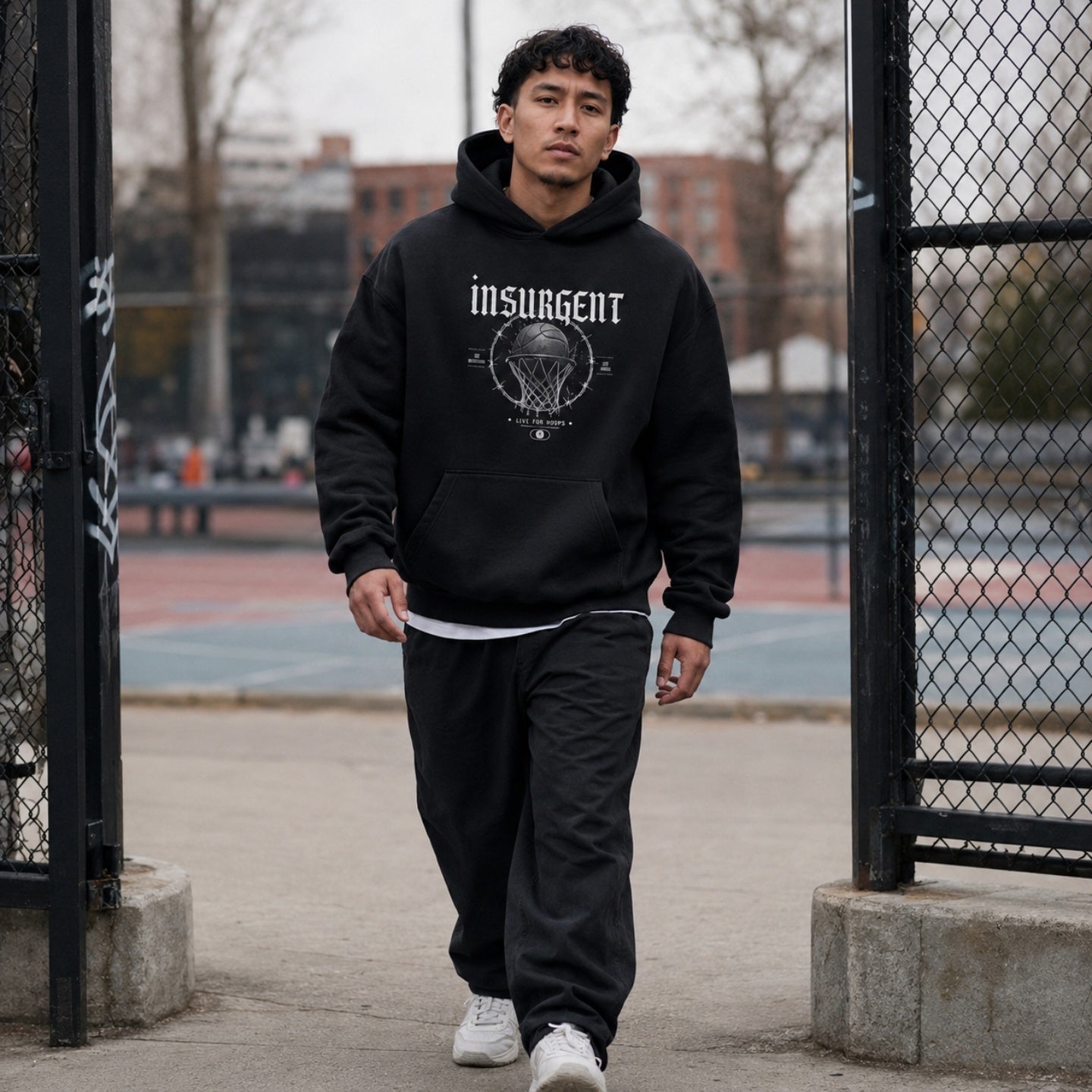 Man wearing Insurgent basketball hoodie front print at an outdoor court gate
