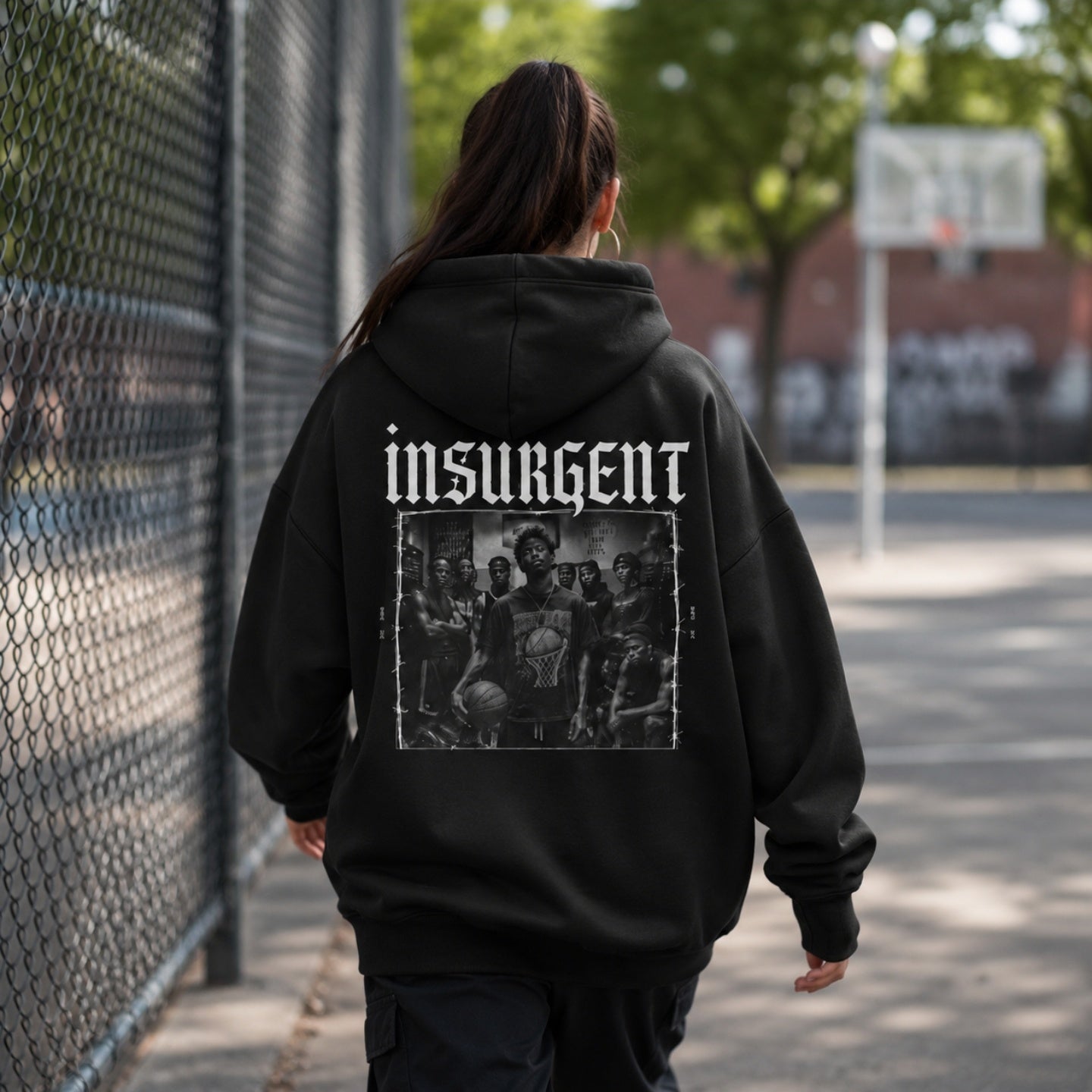 Woman wearing Insurgent hoodie back graphic walking beside a basketball court