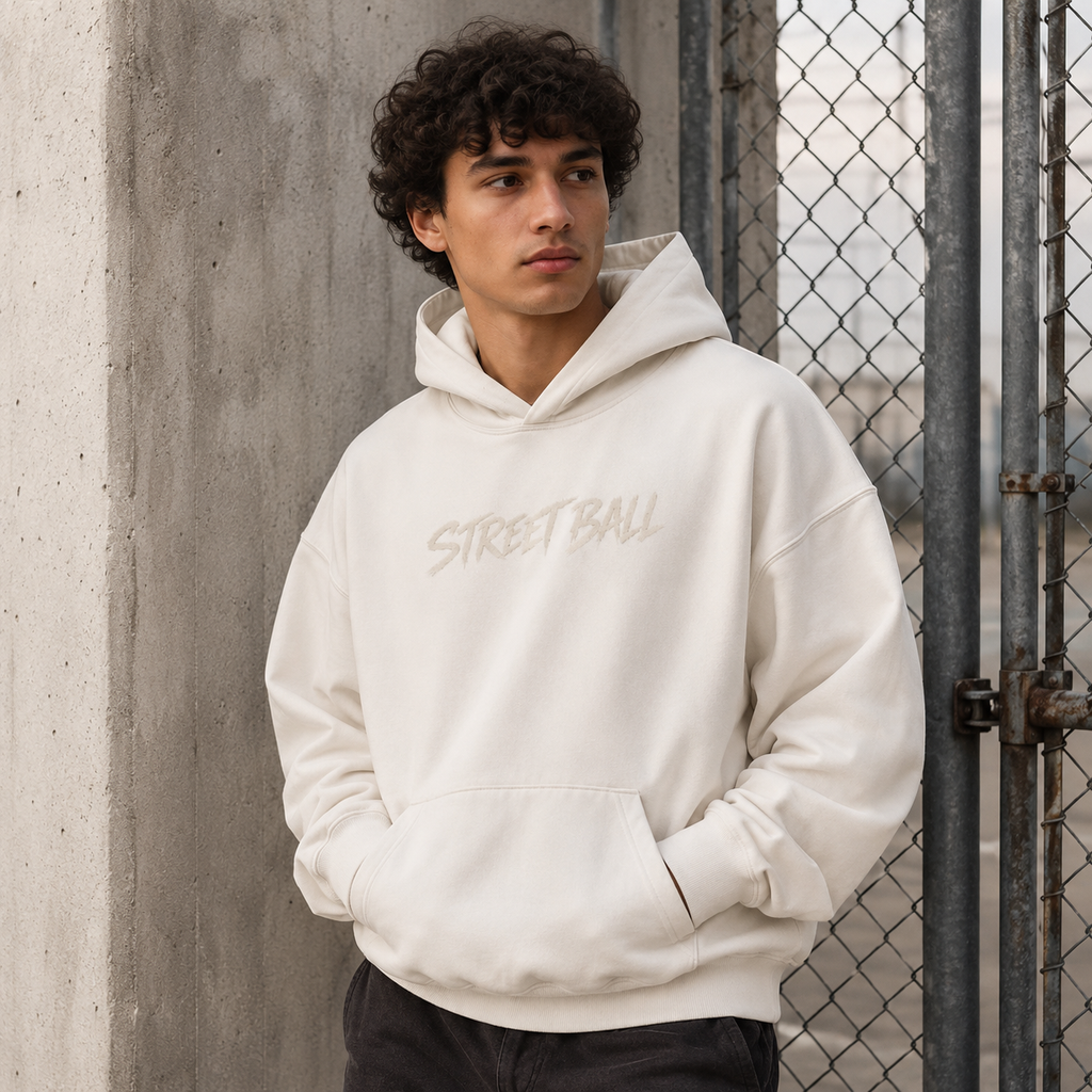 Man wearing light beige Streetball hoodie front print by an industrial fence