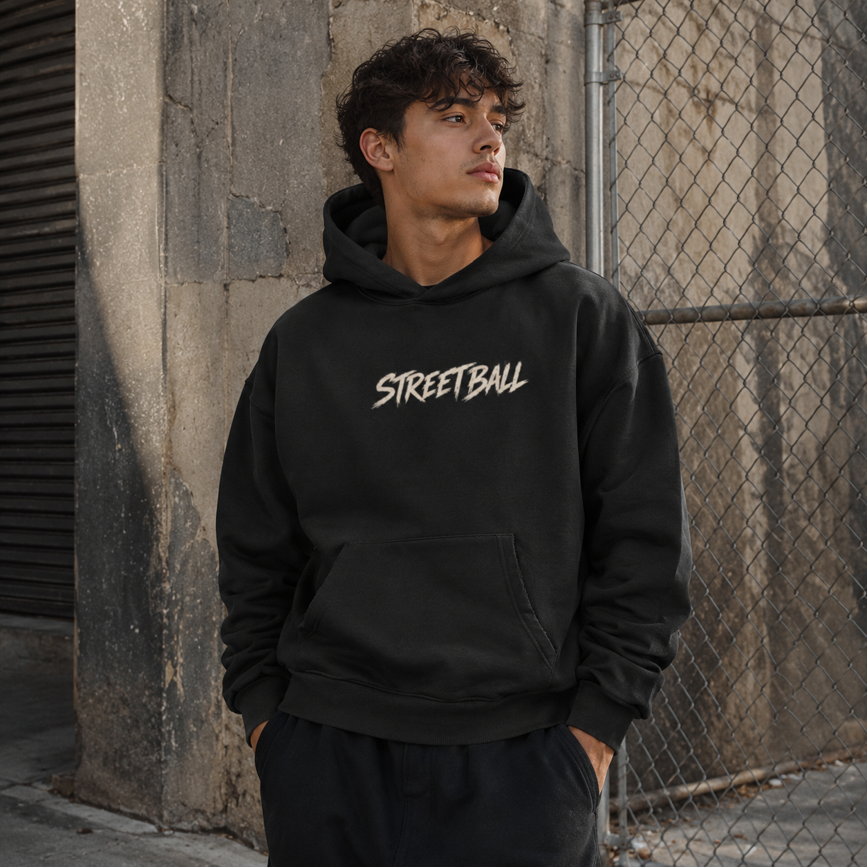 Man wearing black Streetball hoodie front print by a city fence
